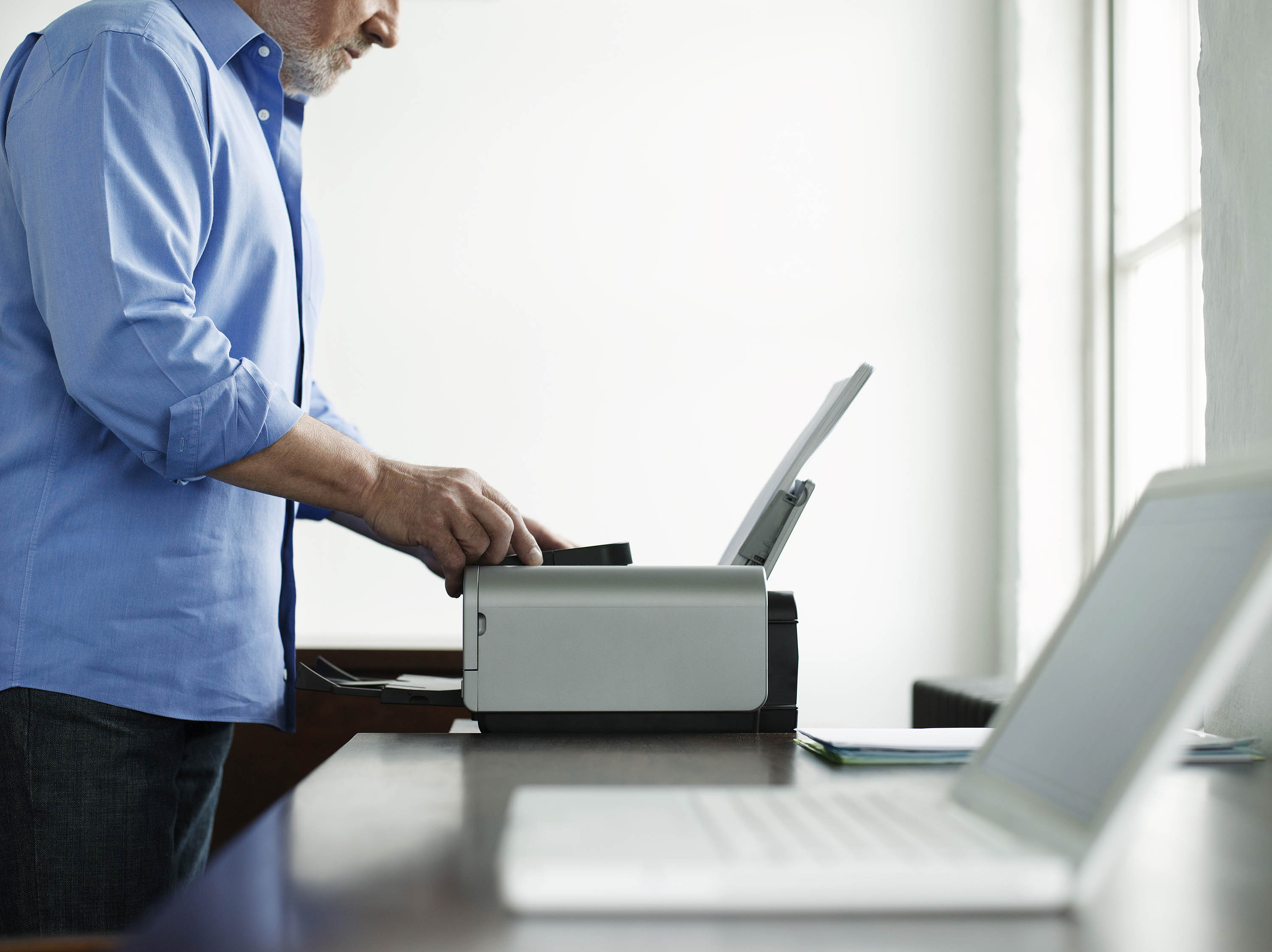 Side view midsection of a mature man using printer at study table in house